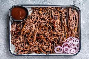 Pulled beef meat with hot chili sauce in baking dish. Gray background. Top view photo