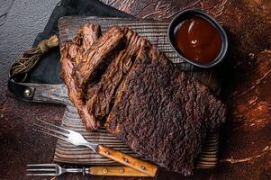 Traditional smoked barbecue wagyu beef brisket on wooden board. Dark background. Top view photo