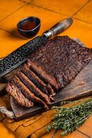 Smoked Barbecue Beef Brisket with Sauce on wooden board. Orange background. Top view photo