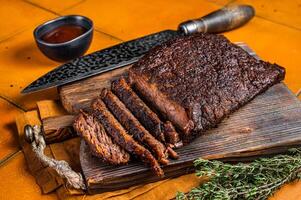 Smoked Barbecue Beef Brisket with Sauce on wooden board. Orange background. Top view photo