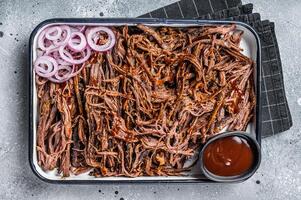 Pulled beef meat with hot chili sauce in baking dish. Gray background. Top view photo