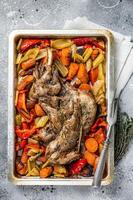 Roast lamb mutton shoulder meat in a baking dish with vegetables. Gray background. Top view photo