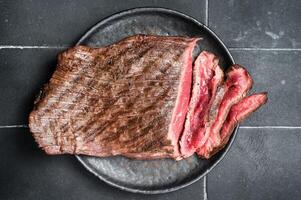 Grilled Flap or Flank Steak, sliced on a plate. Black background. Top view photo