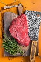 Piece of Raw beef meat for stew with herbs on butcher cutting board. Orange background. Top view photo