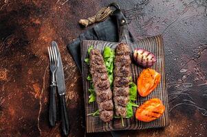 Turkish adana kebab, ground beef and lamb meat grilled on skewers served with tomato, salad and onion. Dark background. Top view photo