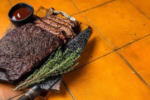 Smoked Barbecue Beef Brisket with Sauce on wooden board. Orange background. Top view. Copy space photo