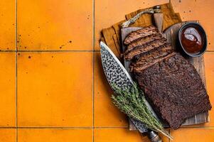 Smoked Barbecue Beef Brisket with Sauce on wooden board. Orange background. Top view. Copy space photo