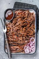 Pulled beef meat with hot chili sauce in baking dish. Gray background. Top view photo