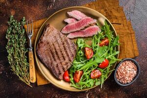 Roasted Flank or Flap Steak in a plate with salad. Dark background. Top view photo