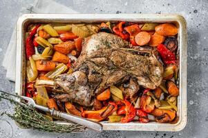 Roast lamb mutton shoulder meat in a baking dish with vegetables. Gray background. Top view photo
