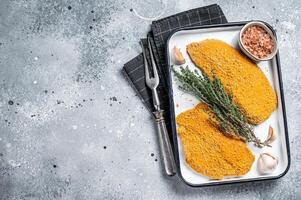 Cooking raw chicken schnitzel in breadcrumbs, uncooked meat steak. Gray background. Top view. Copy space photo