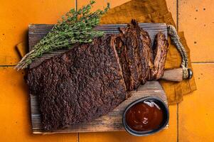 Smoked Barbecue Beef Brisket with Sauce on wooden board. Orange background. Top view photo