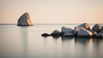 A view of a body of water featuring rocks in the foreground and a rock outcropping nearby. photo