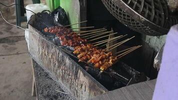 Indonesian man grills chicken satay over charcoal and smoky, with an appetizing look. video