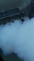 Working premises at elevator plant, thick pipes letting out heavy thick smoke. Flying above the tops of granary silo at the backdrop of grey weather. Vertical video