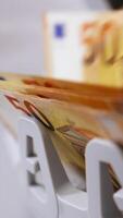 Modern banking activity. Euro banknotes while being counted. Hand of a cashier taking money from counter machine. Close-up. Vertical video