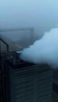 Powerful agribusiness plant for grain storage and processing. Metal tanks and high building with pipes producing thick smoke. Foggy backdrop. Top view. Vertical video