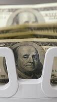 Counting process of dollar banknotes. Automated financial operations. Currency counting machine counts hundred dollar bills. Banking and commercial activity. Close-up. Vertical video