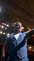Man on stage gesticulating and talk. Professional actor performing his role on spotlight background in theater. View from stage. Vertical video