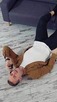 Young man speaking the phone at home. Tired man working through the phone while lying on a floor. Top view. Vertical video