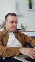 Young man working at home. Relaxed man laying on a sofa and typing on a laptop. Student studying online at home during quarantine. Remote job. Vertical video