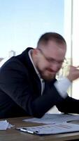 Funny businessman typing on a laptop. Office worker in glasses sitting at his desk in workplace and making mad face. Problems in business. Vertical video