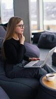 Female freelancer working on a laptop. Beautiful business woman sitting in a comfortable soft chair and typing on a wireless computer. Panoramic window view. Vertical video