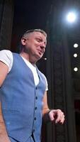 Comedian on stage. Middle-aged speaker standing on stage and talking to someone. Smiling actor rehearses on scene. Vertical video