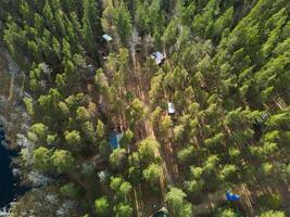 Aerial view of a dense pine forest, rustic cabins, and a nearby water body, creating serenity photo