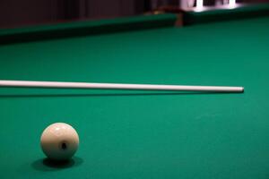 A white cue ball on a green felt pool table, with a cue stick nearby for the next shot photo
