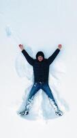 Man lying on snow in winter holiday. Aerial view of snow angel made by man in the snow. Vertical video