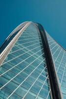A modern skyscraper stands tall against a clear blue sky, captivating onlookers with its design photo