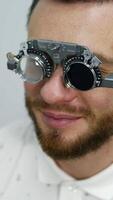 Smiling happy male patient in corrective testing glasses. Checking up eyesight in clinic. Handsome patient in ophthalmology. Vertical video