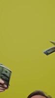 gut aussehend froh Mann mit Geld auf Gelb Hintergrund. zufrieden modern graubärtig Großvater posieren auf Kamera mit viele Dollar Rechnungen. schleppend Bewegung. Vertikale video