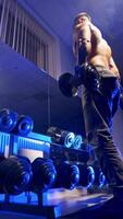 Bodybuilder working out with bumbbells weights at gym. Strong well built bodybuilder lifting dumbbell weights, getting ready for exercise in fitness. Vertical video