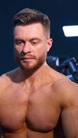 Man with perfect body train muscles on sport equipment and drinks water. View from the side on handsome man with perfect body. Vertical video