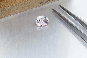 macro mineral faceted stone Morganite with tweezers on a gray background photo