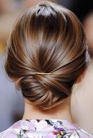 Close up of a sleek low chignon tucked with a gold pin with soft tendrils, back view photo