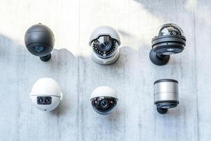Different types of security cameras are displayed on concrete wall. photo