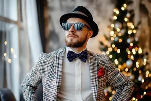 A man in a bow tie and sunglasses standing near a christmas tree photo