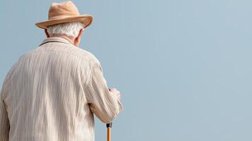 Elder-Focused Healthcare Modern Solutions for Aging. An elderly man in a hat and sweater stands with a cane, gazing into the distance against a clear sky. photo