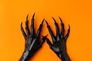Hands of a woman with black claws on an orange background photo