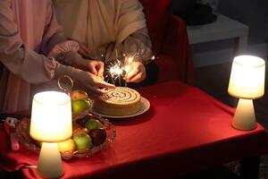 Women celebrate with cake and fireworks at cafe, ignite sparklers on birthday cake, closeup of hand, space for text. photo