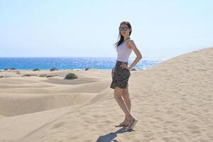 A girlstanding in a model pose on the sand at the background of the sea. Dune in Maspalomas, Gran Canaria. Touristic travel concept photo