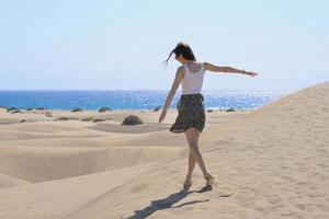 A girl walks along the sand against the background of the sea, rear view. Dune in Maspalomas, Gran Canaria. Touristic travel concept photo