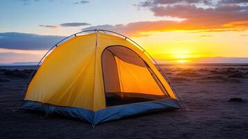 A yellow tent glows warmly as the sun sets, casting colors across the open terrain in the evening light photo