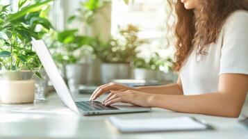 A person works on a laptop, surrounded by greenery and natural light filtering through the window photo