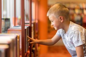 Smart intelligent preschool kid choosing books in school library photo