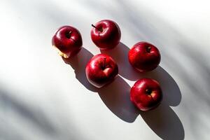 Five red ripe apples lying on a white table and their shadows photo