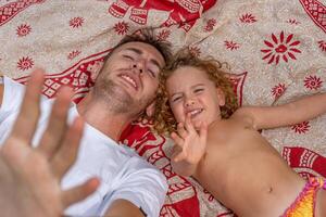 young dad having fun with his little daughter lying on a batik blanket during summer vacation photo